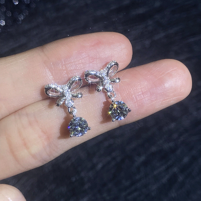 VANLARA bow drop moissanite earrings held on hand with sparkle