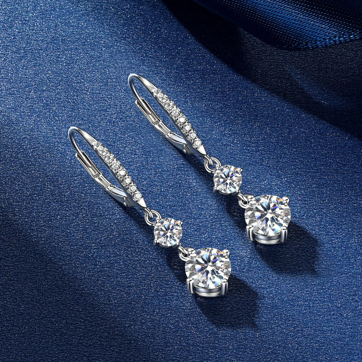 VANLARA double stone moissanite drop earrings angled on blue satin